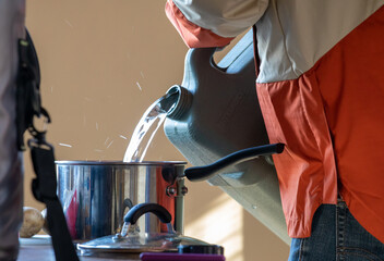Un homme verse de l'eau d'un contenant en plastique à une casserole en métal