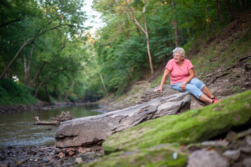 Older Lady sitting on a Rock Near a River