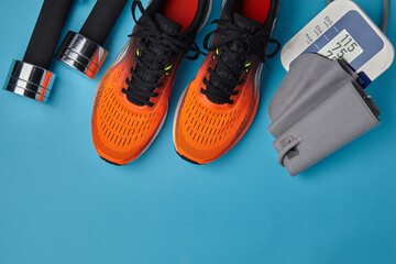 Orange sneakers, dumbbells and blood pressure monitor on a blue background