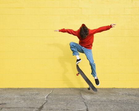 Youth Boy Skating Outside with Yellow Wall