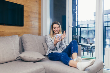 Young beautiful woman sitting at home on the couch and uses a mobile phone, resting from work