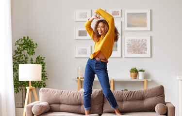 Happy african american teen girl jumping on sofa while having fun on weekend at home