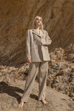 stylish female model standing on beach near rocky cliff