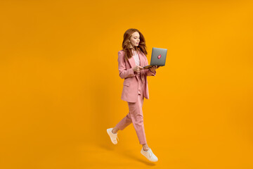 Happy jumping woman with laptop isolated on yellow studio background. Modern technologies, freedom...