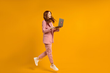 Excited jumping woman with laptop isolated on yellow studio background. Modern technologies, freedom of choices concept, emotions concept. Using laptop for work and fun in flight.