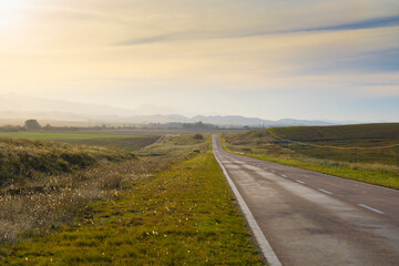 deserted route at sunset road to the mountains covered by a blanket of mist