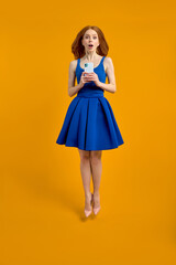 Full size profile photo of surprised redhead female in dress jump use smartphone search discounts run fast, isolated yellow color background in studio, portrait. copy space for advertisement