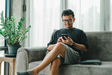 Portrait Happy Asian man using smartphone smiling and relax on sofa living room at home, man using...