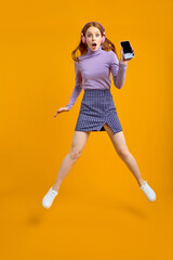 Fototapeta na wymiar Full length body size view of nice cheerful cheery woman in headhones jumping having fun using smartphone fast speed connection, listen to music, isolated on yellow background