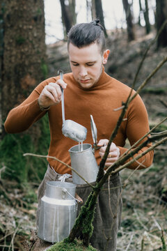 Young Man Pouring Milk With A Ladle In A Pot In The Woods
