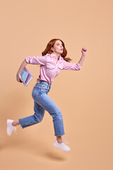 Fototapeta na wymiar Funny redhead female student rushing forwards with book in hands, hurry to university, wearing casual outfit, running, 1 September exam, isolated in studio, full-length portrait