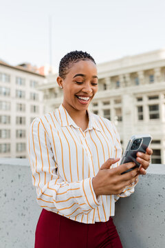Woman Standing on a Building Rooftop in Downtown Laughs While Looking at Her Phone