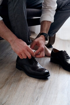 Crop faceless man tying laces on stylish shoes