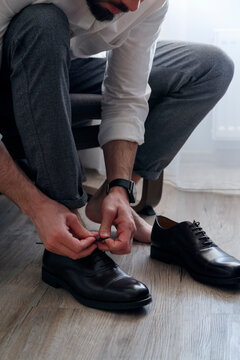 Crop unrecognizable man tying laces on stylish shoes