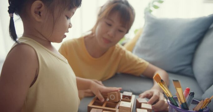 Happy cheerful Asia family mom teach girl play board game hobby with wooden box having fun relax on couch in living room at house. Spending time together, Social distance, Quarantine for coronavirus.
