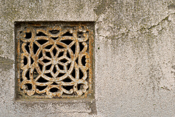 old decorated cast iron ventilation grill of a basement embedded in a wall. Copy space on the right
