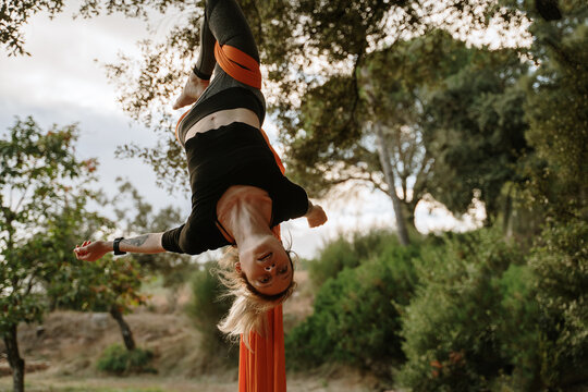 Young woman practicing aerial silks on tree outdoors