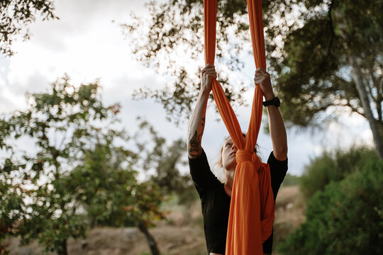 Young woman practicing aerial silks on tree outdoors