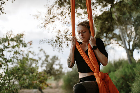 Young woman practicing aerial silks on tree outdoors