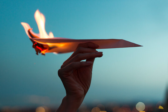 Female hand holding a paper plane on fire