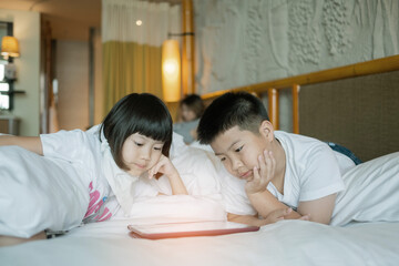 two chinese children addicted tablet, asian child watching telephone together on their bed, kid using smartphone
