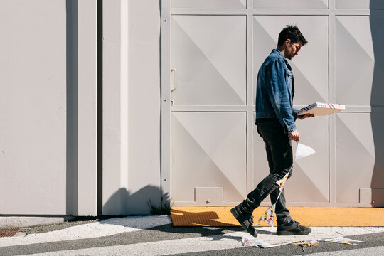 Man in a denim jacket carries a box of pizza