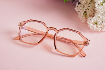 trendy eye glasses and a branch of white lilac on a pink background, eye glasses and flowers