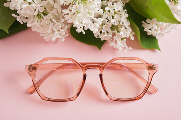 trendy eye glasses and a branch of white lilac on a pink background, eye glasses and flowers