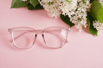 Obraz na płótnie Canvas trendy eye glasses and a branch of white lilac on a pink background, eye glasses and flowers