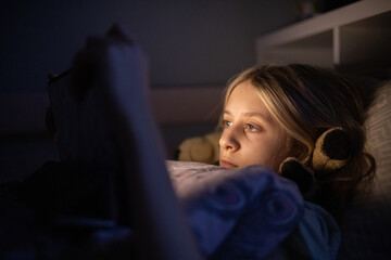 little girl lying in bed watching a movie