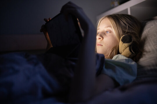 little girl lying in bed watching a movie