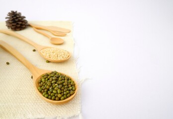 Whole grains such as mung beans, white sesame on wooden spoon and sackcloth on white background.