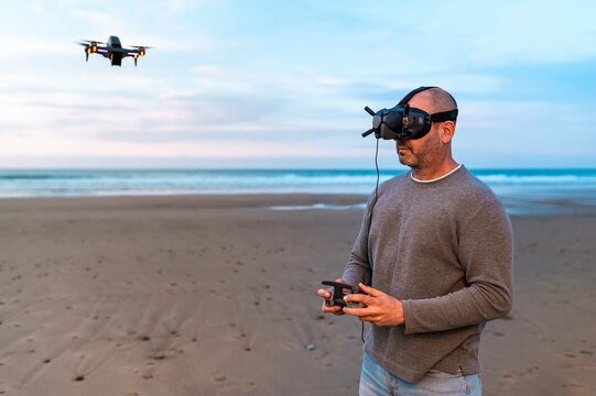 Man controlling drone flying over beach at sunset 