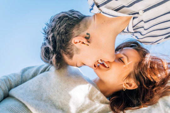 Smiling lesbian women about to kiss against blue sky