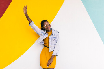 Cheerful stylish woman waving hand near bright wall in city