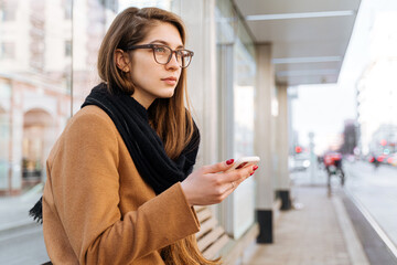 woman at a tram stop with a smartphone in her hands