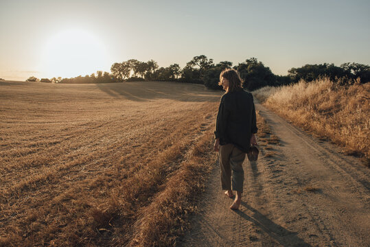 Woman walking on a gravel road going through a field at sunset