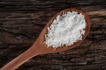 Grated dry coconut in wooden spoon on rustic wooden background.