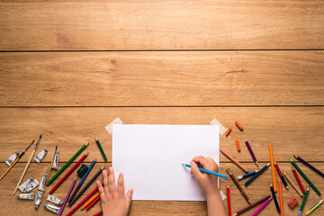 The little boy's hand is about to draw and around. There are many different wood colors and watercolor painting tools. Such as paint tubes and paintbrushes Placed on a wooden table, with copy space.