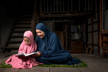 Grandmothers and little niece, Asiatic Muslims, are sitting and teaching to read the quran in a...