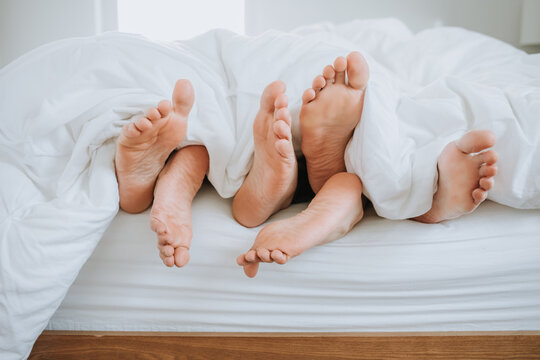 Closeup of Three Pairs of Feet in Bed