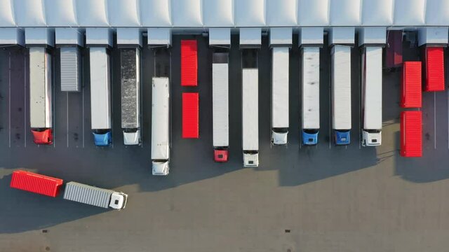 Aerial top down view of semi-trailer trucks standing at a warehouse ramps for loading and unloading goods  in a logistics park
