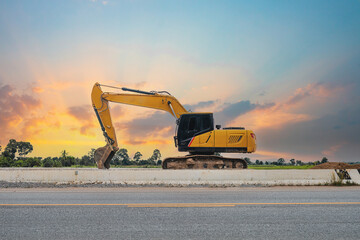 A yellow backhoe parked on the roadside in the sky at sunset.