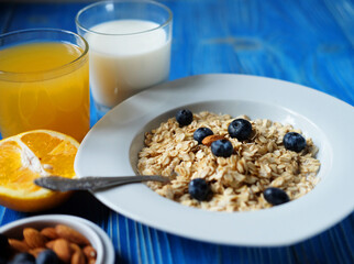 oatmeal with fresh berries on white plate with orange juice and milk,