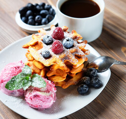A cup of coffee and Belgian waffles with strawberry ice cream, fresh raspberries and mint