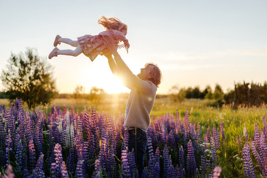 Father tossing daughter in flower field at sunset