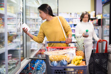 Female shopper pulls dairy products out of the refrigerator at a grocery supermarket