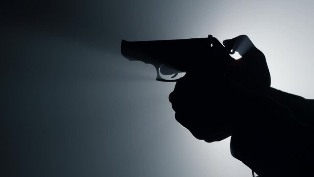 Silhouette male hand cocking gun trigger. Unknown criminal cocking trigger.
