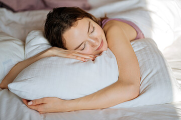 happy woman hugging pillow while lying in bed