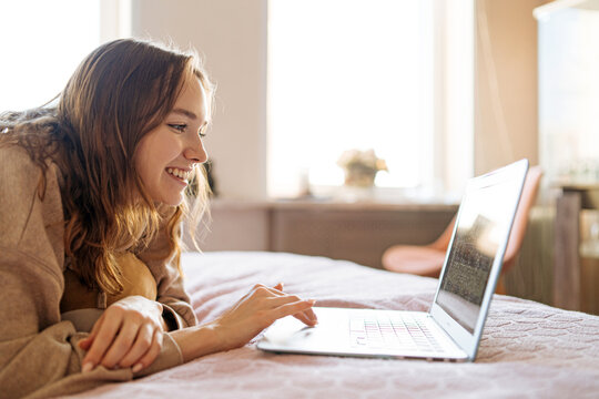 
smiling girl looking at laptop while lying in bed
